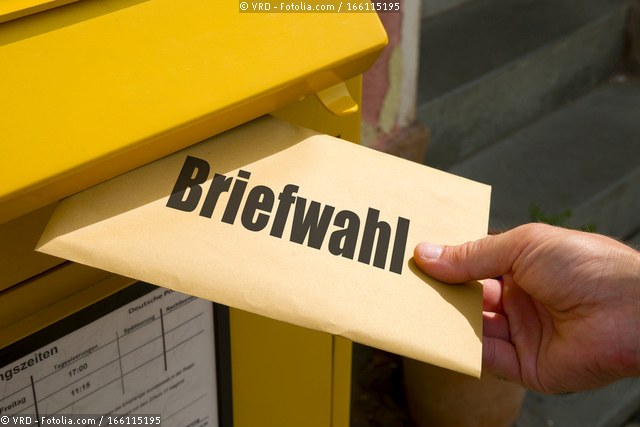 Dieses Bild zeigt einen Briefkasten, in dem ein Wahlbriefumschlag eingeworfen wird. © VRD - Fotolia.com / 166115195